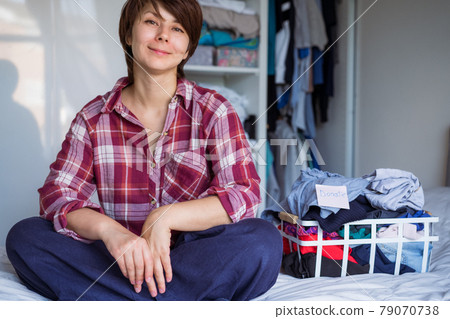 Smiling Woman with selected clothes from her wardrobe for donating to a Charity. Decluttering Clothes, Sorting, And Cleaning Up. Reuse, second-hand concept. Conscious consumer, sustainability. 79070738