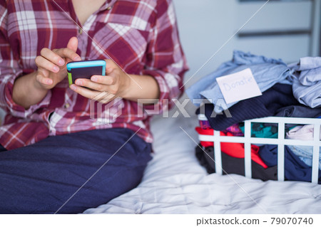 Close up woman using her smartphone to find places where to donate her clothes. Decluttering Clothes, Sorting, And Cleaning Up. Conscious consumer, sustainability. Reuse, second hand, Charity concept. 79070740
