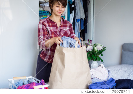 A Woman selecting clothes from her wardrobe for recycle or donating to a Charity shop. Woman Decluttering Clothes, Sorting, And Cleaning Up. Reuse, second-hand. Conscious consumer, sustainability. A Woman selecting clothes from her wardrobe for recycle or donating to a Charity shop. Woman Decluttering Clothes, Sorting, And Cleaning Up. Reuse, second-hand. Conscious consumer, sustainability. 79070744