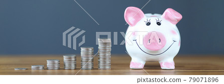 Pink piggy bank standing on table near heaps of coins 79071896
