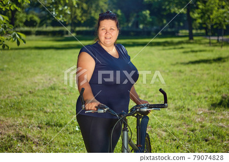 Stout mature woman on bike ride in public park on sunny summer day. 79074828