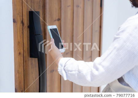 The hand holding the smartphone over the entrance door 79077716