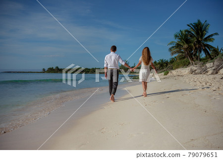 A man and a woman walk on the seashore and look at the horizon. 79079651