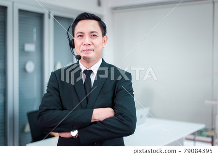 Portrait of call center asian man operator standing with headset looking to camera at office 79084395