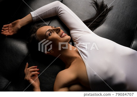 Smiling woman in bodysuit on leather couch in studio Smiling woman in bodysuit on leather couch in studio 79084707
