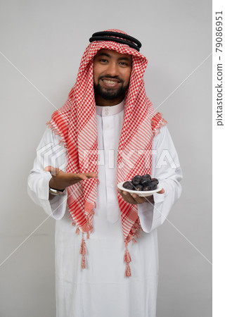 An Arab in a turban smiles while carrying a plate of dates with the other hand offering it An Arab in a turban smiles while carrying a plate of dates with the other hand offering it 79086951