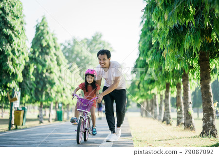 Father Teaching daughter To Ride Bike In the park Father Teaching daughter To Ride Bike In the park 79087092