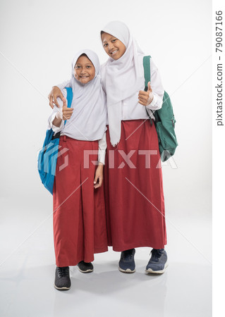 two smiling girls wearing hooded elementary school uniforms with thumbs up and a school bag 79087166