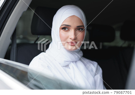 Beautiful muslim woman in white hijab sitting on the back seat of a luxury car Beautiful muslim woman in white hijab sitting on the back seat of a luxury car 79087701