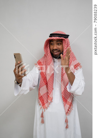 an arabian youth in a turban makes a video call using a mobile phone while smiling with a hand gesture 79088239
