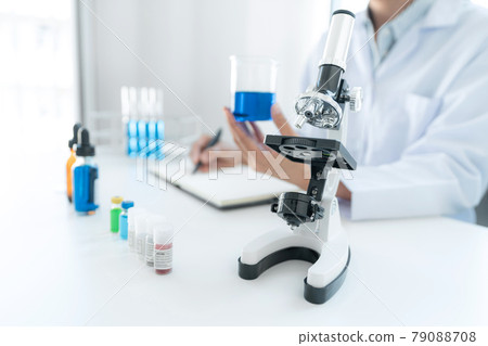 Scientist woman holding beaker in his hands and writing down result report on notebook while working 79088708