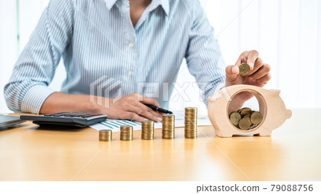 Asian business woman putting coin on stack coin and holding coin putting into piggy bank on the table Asian business woman putting coin on stack coin and holding coin putting into piggy bank on the table 79088756