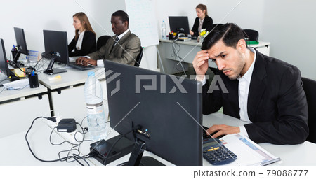 Upset Hispanic businessman worriedly looking at computer monitor in modern open plan office Upset Hispanic businessman worriedly looking at computer monitor in modern open plan office 79088777