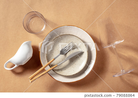 Modern tableware set. Ceramic plates, a wine glass, and cutlery Modern tableware set. Ceramic plates, a wine glass, and cutlery 79088864