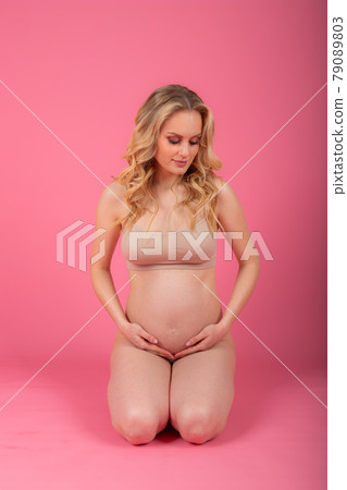 beautiful young pregnant woman sitting on the floor, on a pink studio background beautiful young pregnant woman sitting on the floor, on a pink studio background 79089803