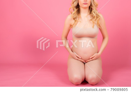 beautiful young pregnant woman sitting on the floor, on a pink studio background beautiful young pregnant woman sitting on the floor, on a pink studio background 79089805