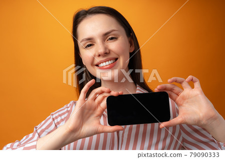 Happy smiling young woman showing you black smartphone screen with copy space 79090333