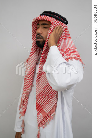 An Arab muezzin in a turban performs the call to prayer with one hand beside his ear 79090334
