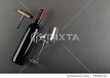 Corked red wine bottle, corkscrew and empty wine glass on gray background. Corked red wine bottle, corkscrew and empty wine glass on gray background. 79090522