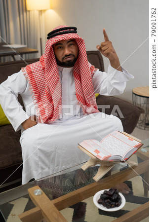 a serious arab young man while reading the quran on the table with hands expression a serious arab young man while reading the quran on the table with hands expression 79091762