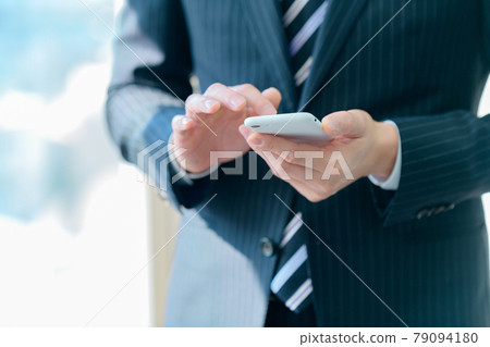 A businessman in a suit operating a smartphone in the office A businessman in a suit operating a smartphone in the office 79094180