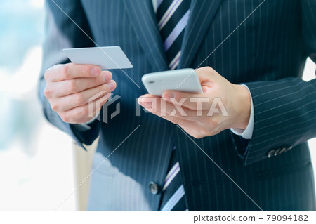 A businessman in a suit with a smartphone that makes card payments in the office 79094182