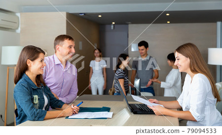 Smiling young woman assistant of notary public receiving customers in hall of modern office Smiling young woman assistant of notary public receiving customers in hall of modern office 79094533