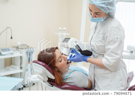 Attractive smiling woman doctor in a white uniform with tools in hand. Young beautiful female dentist takes jaw x-ray of female patient. Attractive woman patient at dentist taking x-ray exam. Attractive smiling woman doctor in a white uniform with tools in hand. Young beautiful female dentist takes jaw x-ray of female patient. Attractive woman patient at dentist taking x-ray exam. 79094871