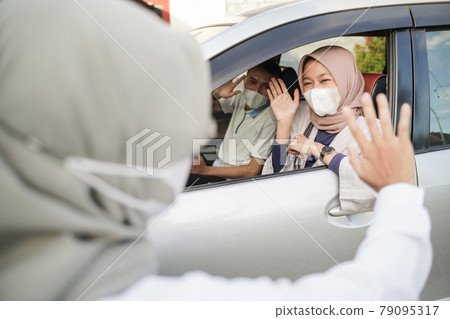Muslim couple wearing masks waving from inside the car to a woman wearing a hijab Muslim couple wearing masks waving from inside the car to a woman wearing a hijab 79095317