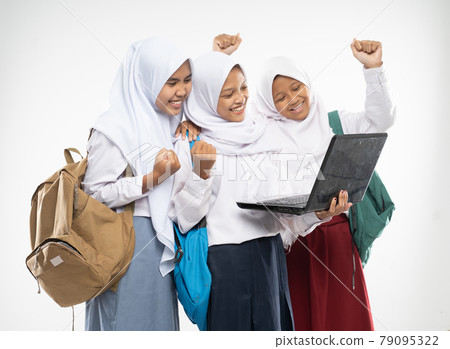 three asian in veils wearing school uniforms stand using a laptop together with excited gestures and raise hands with carrying backpacks 79095322