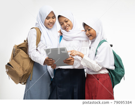 three asian girls in veils in school uniforms stand smiling using a tablet digital while carrying backpacks three asian girls in veils in school uniforms stand smiling using a tablet digital while carrying backpacks 79095384