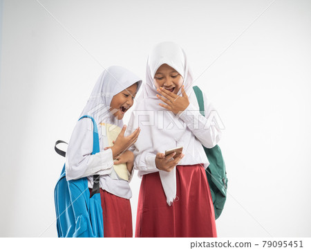 two veiled girls wearing elementary school uniforms using a mobile phone together with shocked expression two veiled girls wearing elementary school uniforms using a mobile phone together with shocked expression 79095451