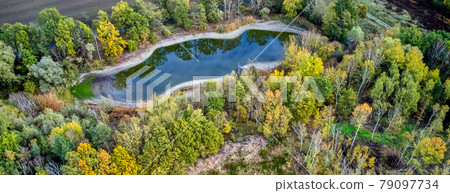Aerial photograph from a height of one hundred metres onto an artificial blue-green pond with trees surroundingin which the clouds are reflected. Aerial photograph from a height of one hundred metres onto an artificial blue-green pond with trees surroundingin which the clouds are reflected. 79097734