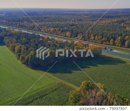 View from a height of 100 meters over the flat landscape in northern Germany with a canal and a canal ship transporting containers. View from a height of 100 meters over the flat landscape in northern Germany with a canal and a canal ship transporting containers. 79097807