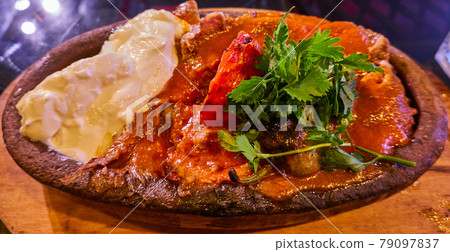 Iskender Kebap, grilled meat from a spit with soaked Turkish flat bread under a thick layer of tomato sauce with a large splash of yoghurt, garnished with parsley on a clay plate Iskender Kebap, grilled meat from a spit with soaked Turkish flat bread under a thick layer of tomato sauce with a large splash of yoghurt, garnished with parsley on a clay plate 79097837