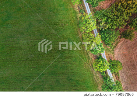 Abstract aerial photograph of a meadow next to a sloping path at the edge of a group of trees Abstract aerial photograph of a meadow next to a sloping path at the edge of a group of trees 79097866