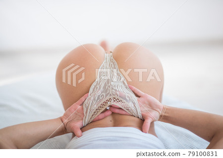 Beautiful sporty European girl in elegant light panties and a white t-shirt. A woman with attractive buttocks in lace underwear adjusts her panties with her hands. 79100831