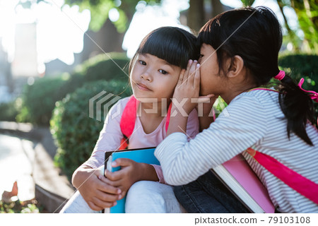 little girl student whispering to her friend. little girl student whispering to her friend. 79103108