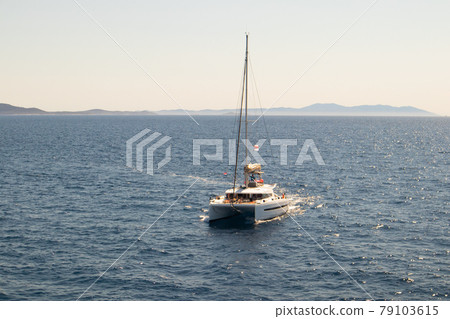 Double-decked catamaran, a yacht with lowered sails, looking towards the horizon. The azure ocean on a sunny day off the coast of Croatia Double-decked catamaran, a yacht with lowered sails, looking towards the horizon. The azure ocean on a sunny day off the coast of Croatia 79103615