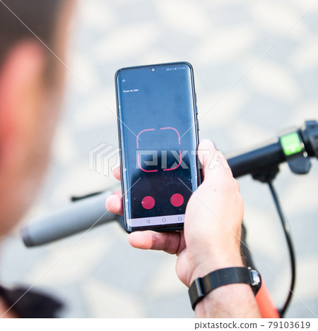 Close up of hand and smartphone, unlocking dockless electric scooter for rent with debranded generic phone app. 79103619