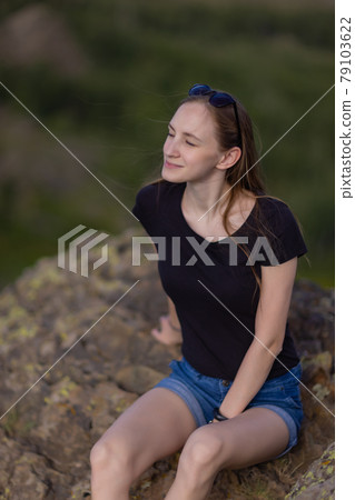 Female hiker with backpack sitting on top of the mountain enjoying the view during the day. 79103622