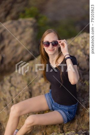 Female hiker with backpack sitting on top of the mountain enjoying the view during the day. 79103623