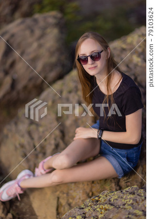 Female hiker with backpack sitting on top of the mountain enjoying the view during the day. 79103624