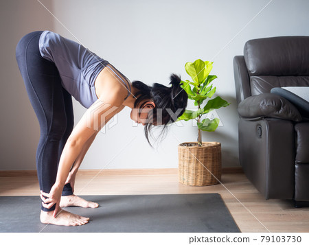 Uttanasana Standing Forward Bend yoga pose asian woman home workout fitness body exercise health training sport healthy lifestyle activity wellness care on mat indoors natural light selective focus 79103730
