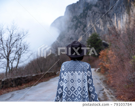 Stylish hipster woman in a hat walking down a mountain road 79103784