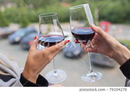 Two people clinking with glasses of red wine, celebrating success or speaking toast in wine restaurant, against racks with wine bottles, close up. Two people clinking with glasses of red wine, celebrating success or speaking toast in wine restaurant, against racks with wine bottles, close up. 79104276