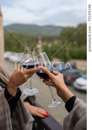 Two people clinking with glasses of red wine, celebrating success or speaking toast in wine restaurant, against racks with wine bottles, close up. Two people clinking with glasses of red wine, celebrating success or speaking toast in wine restaurant, against racks with wine bottles, close up. 79104296