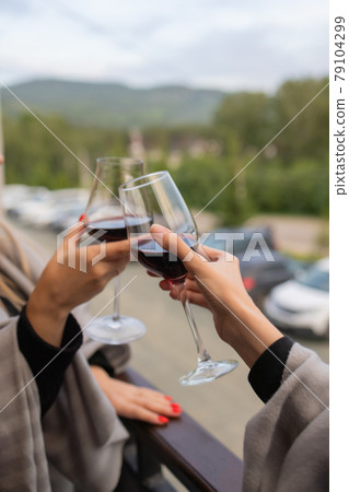 Two people clinking with glasses of red wine, celebrating success or speaking toast in wine restaurant, against racks with wine bottles, close up. Two people clinking with glasses of red wine, celebrating success or speaking toast in wine restaurant, against racks with wine bottles, close up. 79104299