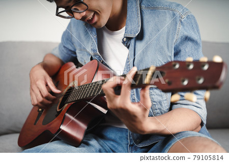 Enjoy handsome asian man practicing or playing the guitar on the sofa at living room Enjoy handsome asian man practicing or playing the guitar on the sofa at living room 79105814