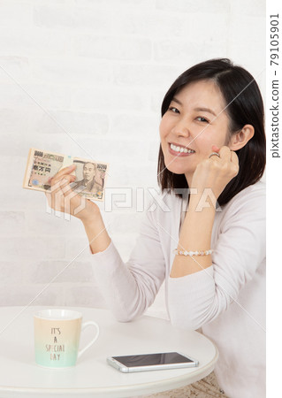 一位年輕女子通過智能手機信息賺了很多錢，手裡拿著一疊鈔票 79105901